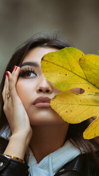 Kobieta z jesiennym liściem przy twarzy