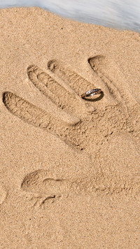 Odcisk dłoni z pierścionkiem na piasku