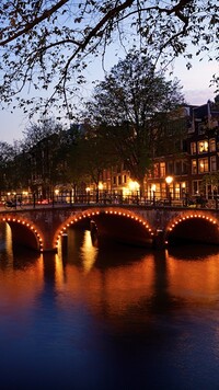 Oświetlone domy i most nad kanałem w Amsterdamie