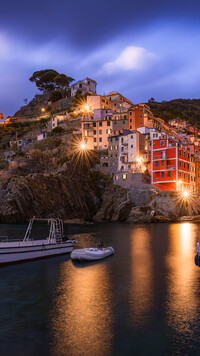 Oświetlone domy w Riomaggiore i łodzie w zatoce
