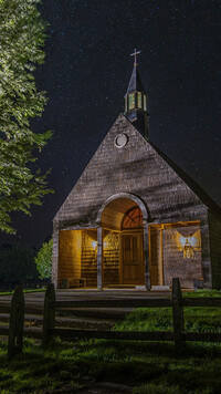 Oświetlony drewniany kościół pod gwiaździstym niebem