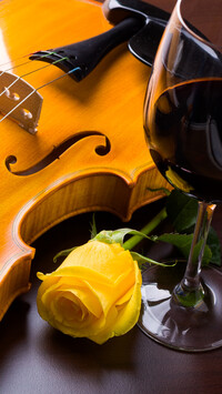 Skrzypce obok żółtej róży i kieliszka wina