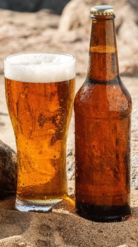 Szklanka z piwiem obok butelki na piasku