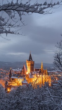 Widok zza ośnieżonych drzew na oświetlony Zamek Wernigerode