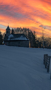 Zachód słońca nad kościołem na ośnieżonym wzgórzu
