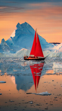 Żaglówka z czerwonym żaglem obok góry lodowej
