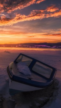 Zamarznieta motorówka na jeziorze zimą o zachodzie słońca.
