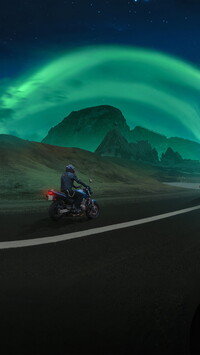 Zorza polarna nad górami i motocyklista na drodze