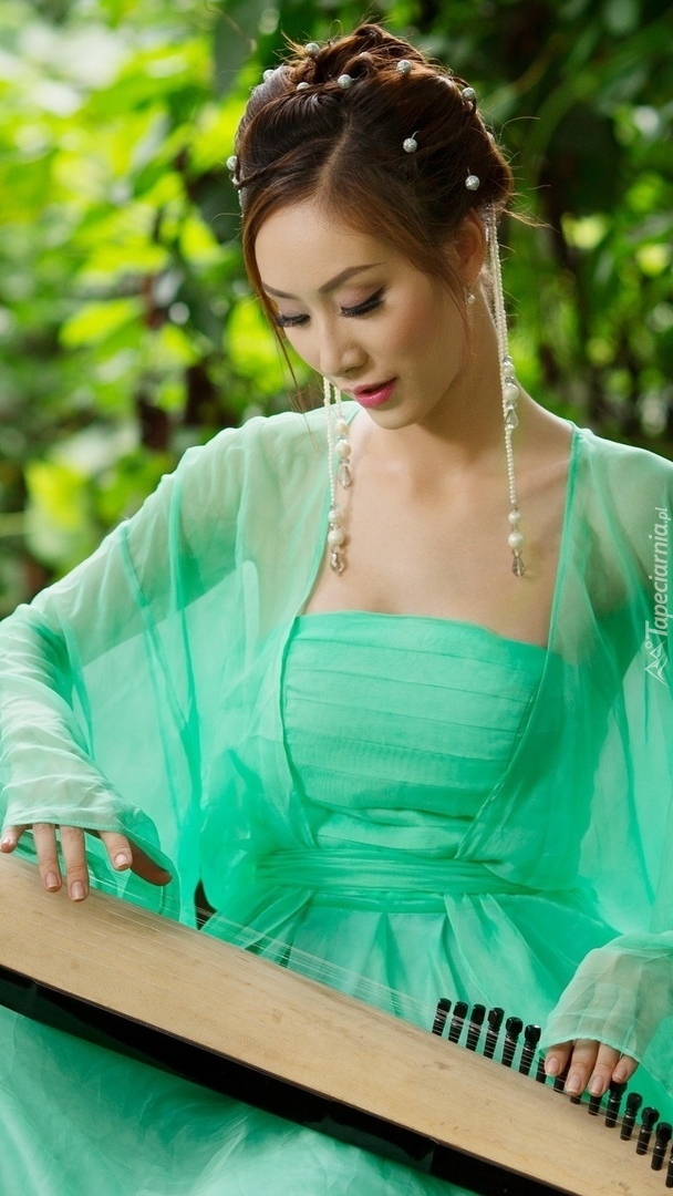 Azjatka w zielonej sukience grająca na koto