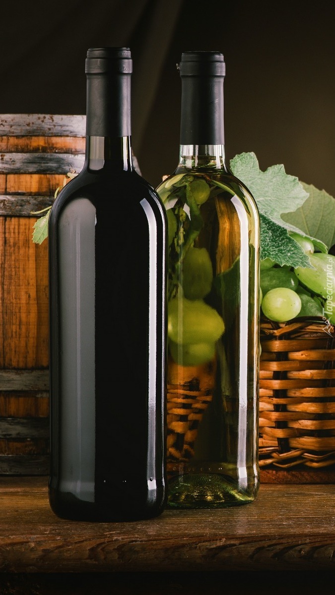 Butelki wina obok beczki i koszyka winogron