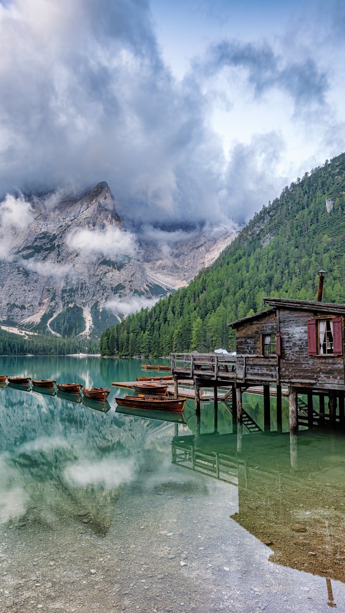 Domek i łodzie na jeziorze Lago di Braies w zamglonych Dolomitach