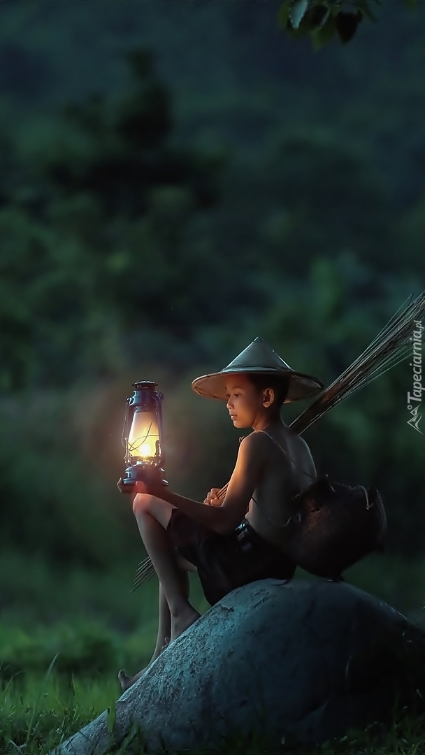 Dziecko z lampą siedzi na kamieniu