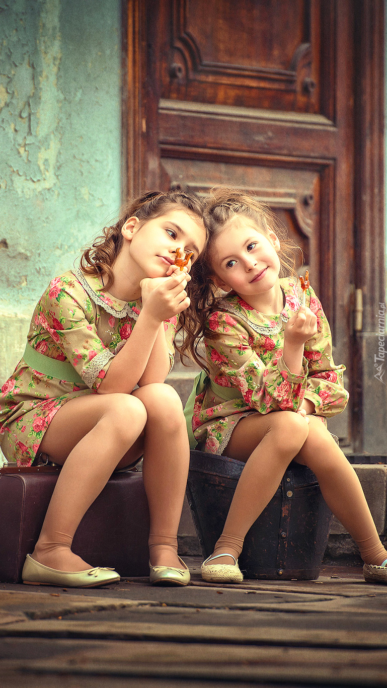 Dziewczynki siedzą przed drzwiami ze słodkimi lizakami