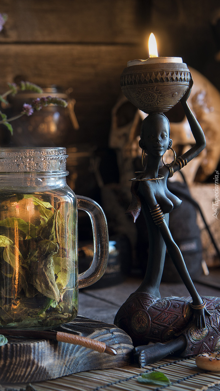 Figurka ze świecą obok słoika z herbatą miętową