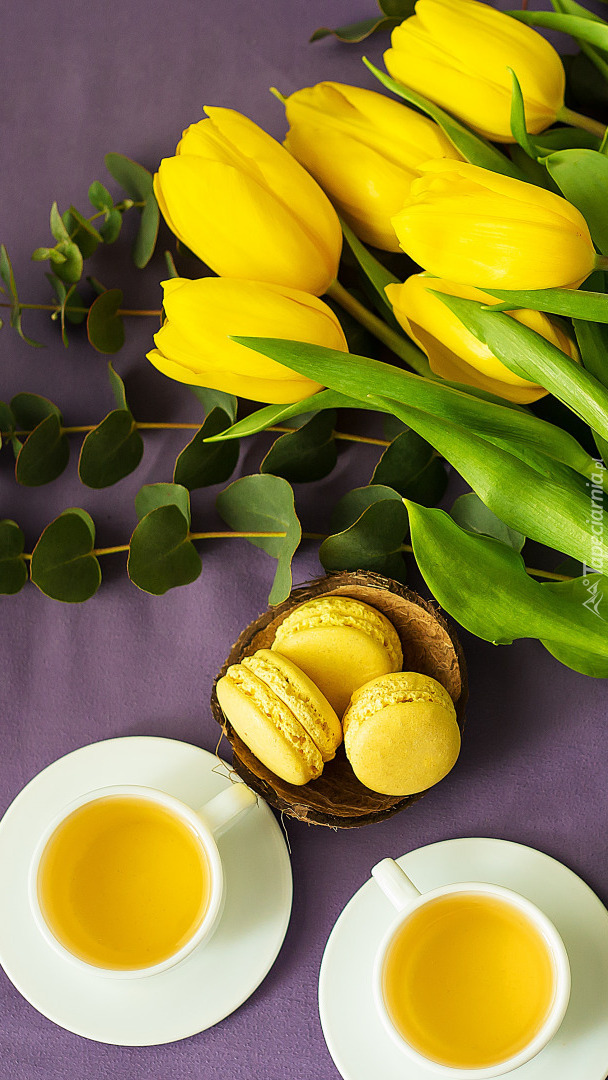 Filiżanki herbaty i makaroniki obok żółtych tulipanów