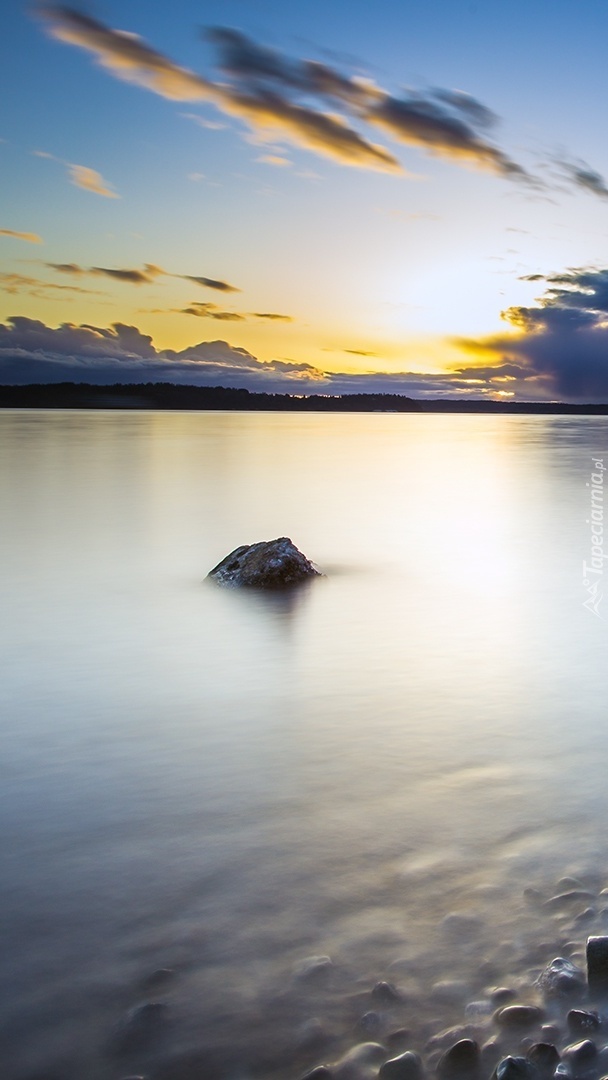 Jezioro z kamieniami przy brzegu o zachodzie słońca