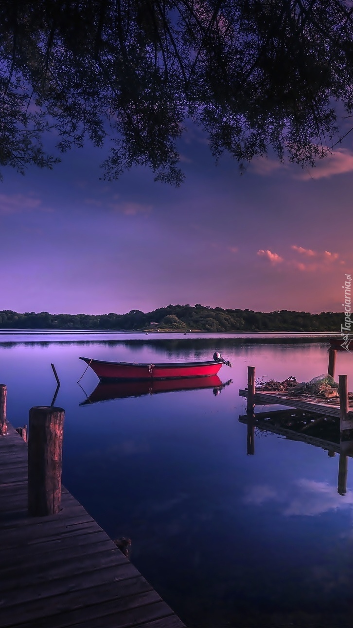 Jezioro z pomostem i łódką o zachodzie słońca