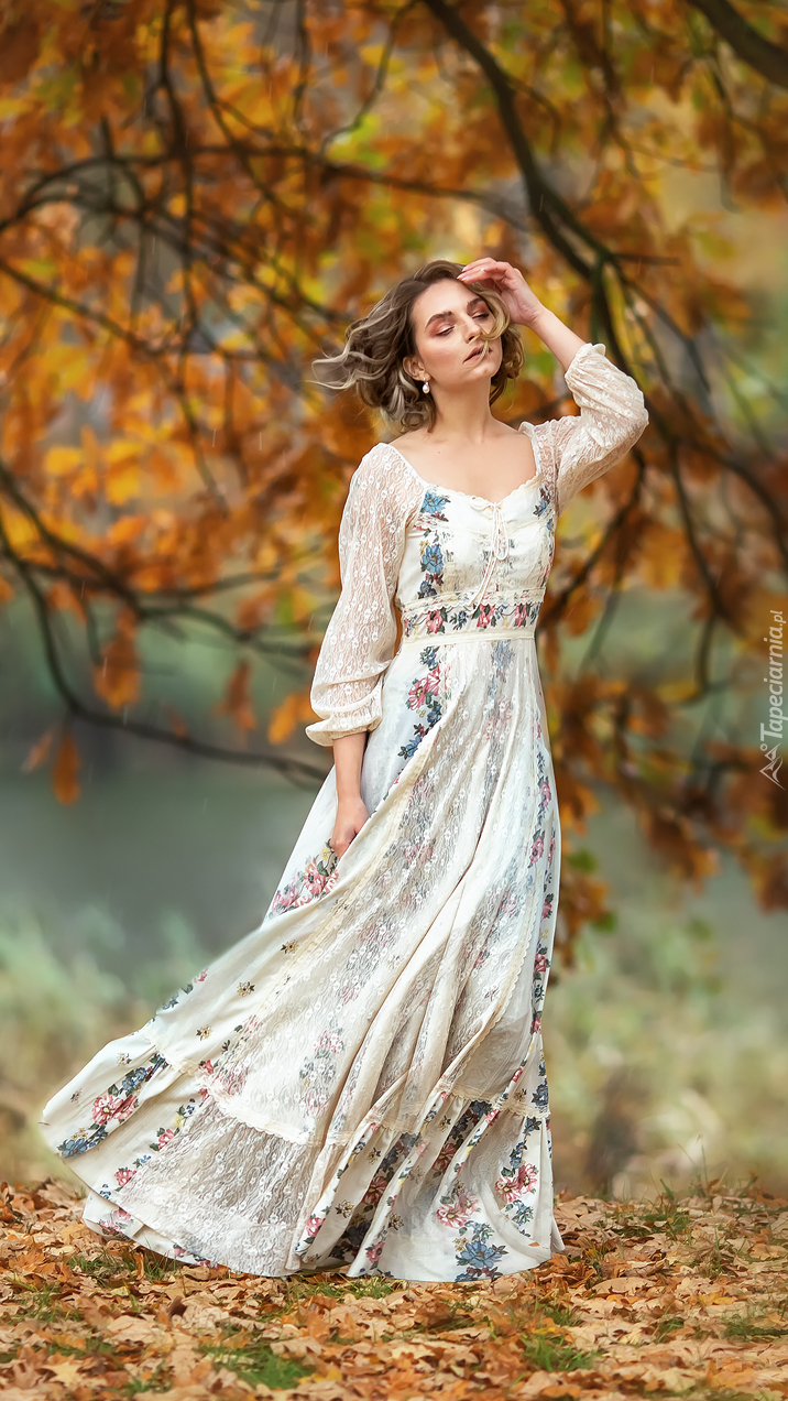 Kobieta w długiej sukni pod jesiennym drzewem