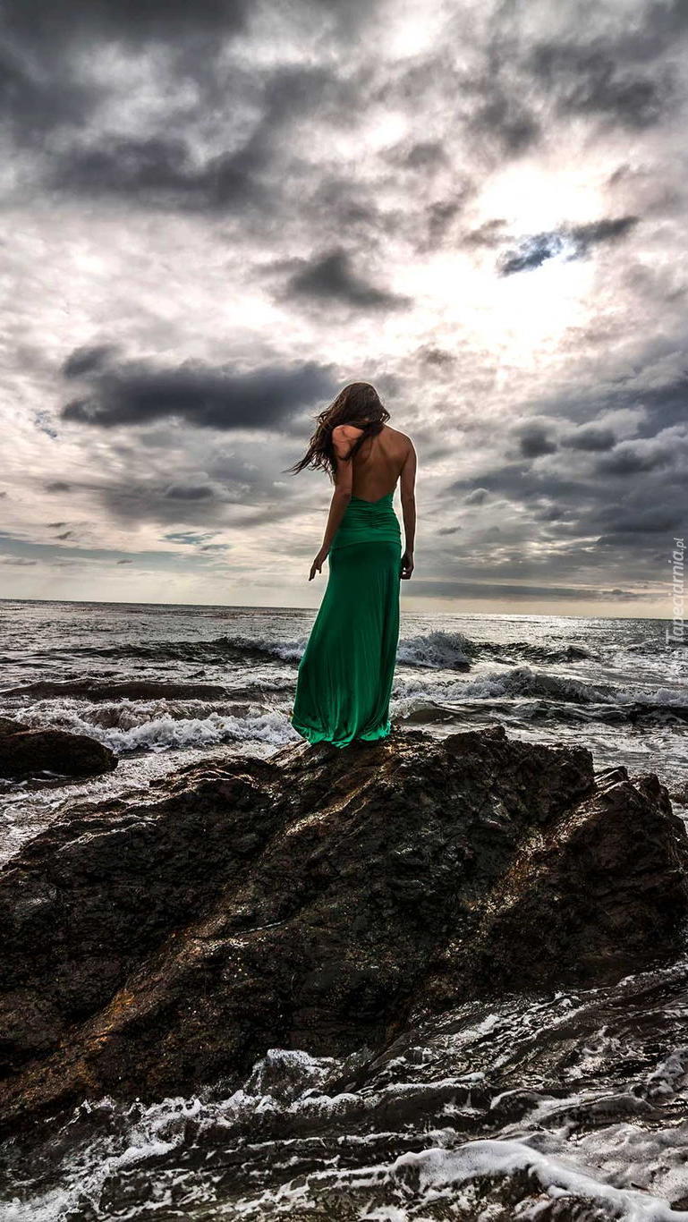 Kobieta w zielonej sukni na skale otoczonej morzem