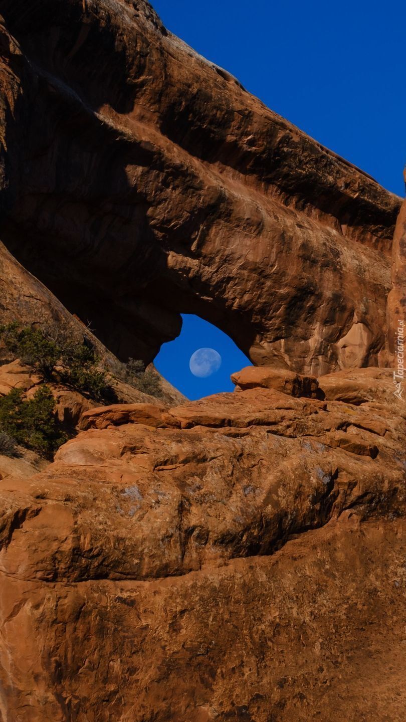 Księżyc na błękitnym niebie za skałami