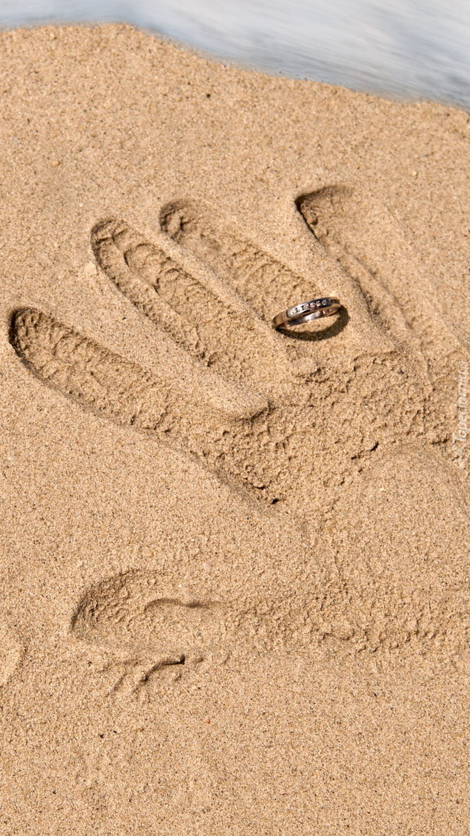 Odcisk dłoni z pierścionkiem na piasku