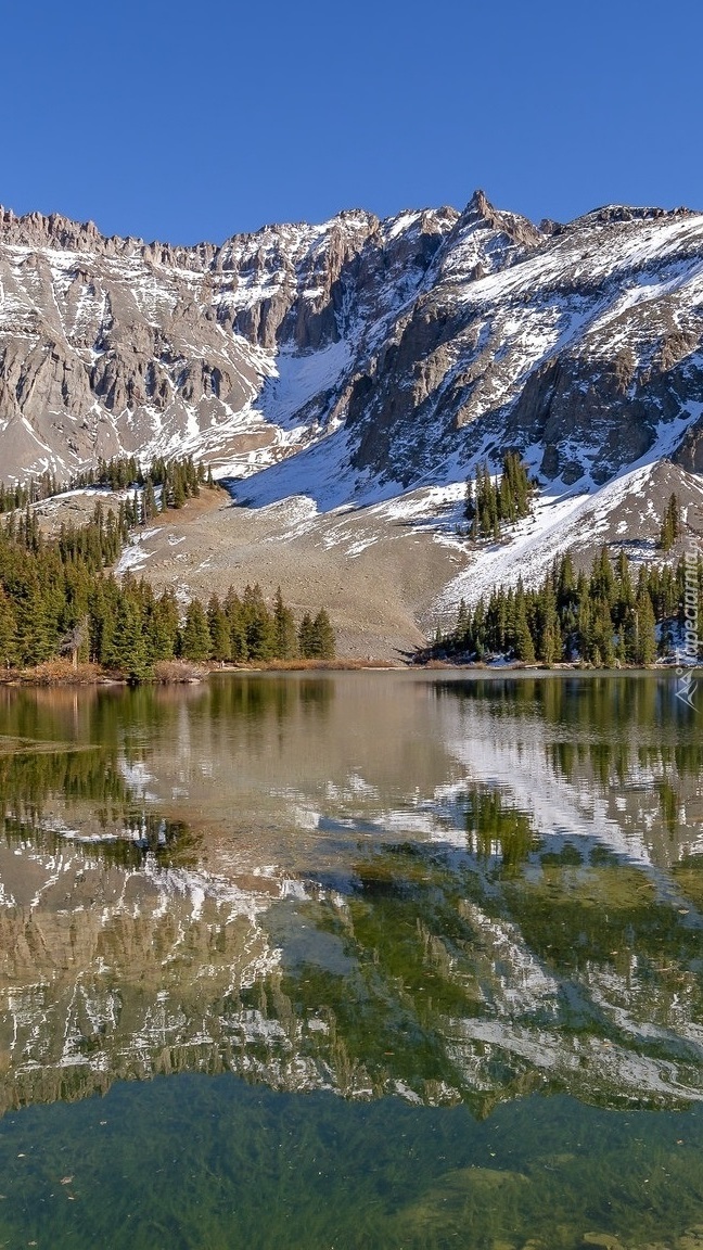 Ośnieżone góry i świerki nad jeziorem