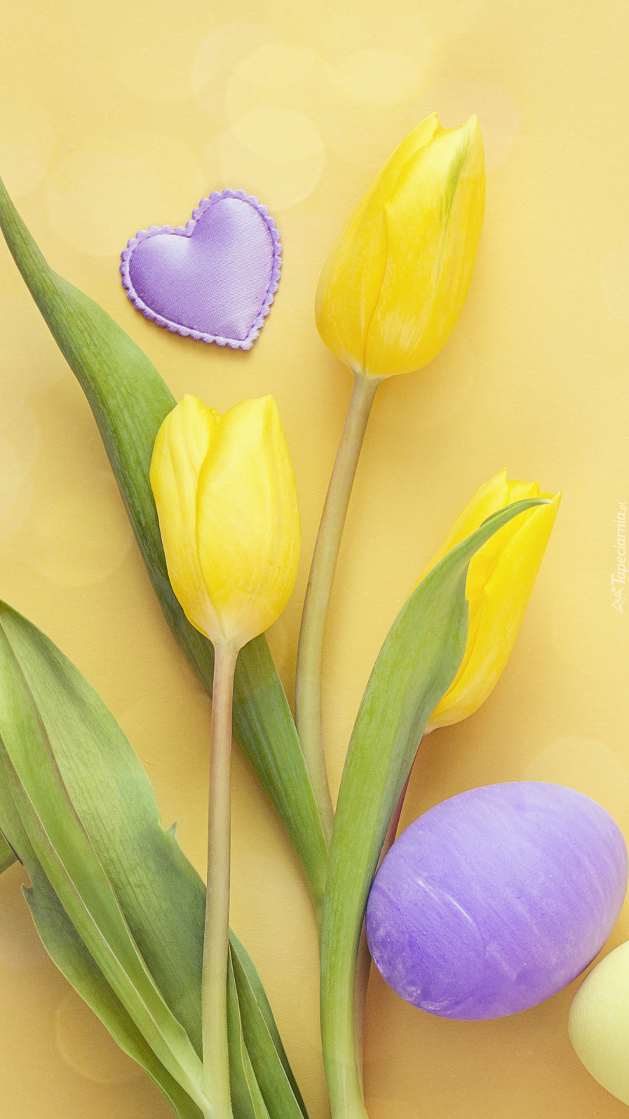 Pisanki i serduszko obok żółtych tulipanów
