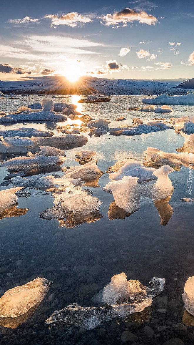 Promienie słońca muskają bryły lodu nad jeziorem w Islandii