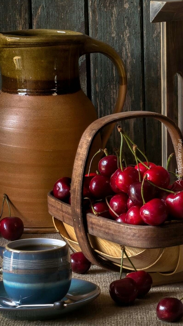 Wiśnie w koszyku obok dzbanka i filiżanki