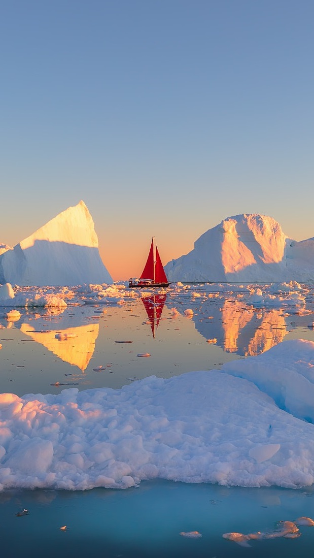 Żaglówka z czerwonymi żaglami i góry lodowe na morzu