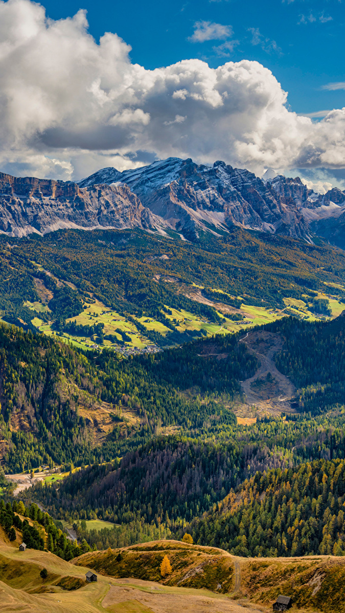 Zalesiona dolina Val Badia i Dolomity pod białymi chmurami w Południowym Tyrolu