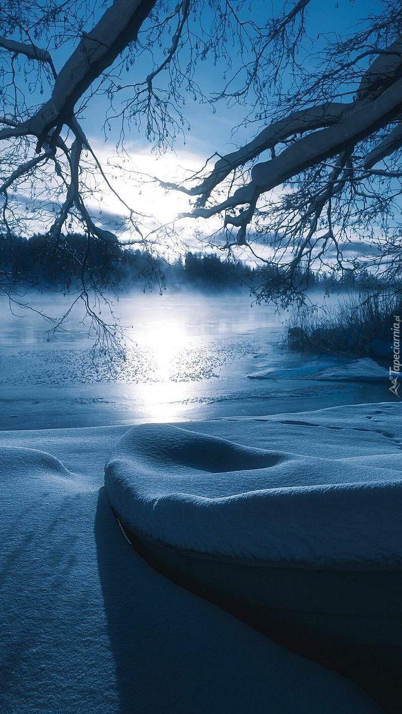 Zaśnieżona łódka na brzegu jeziora