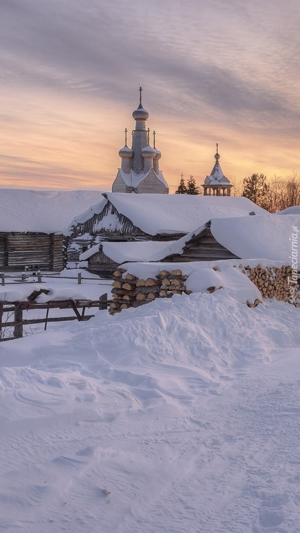 Zasypane śniegiem szopy i cerkiew w tle