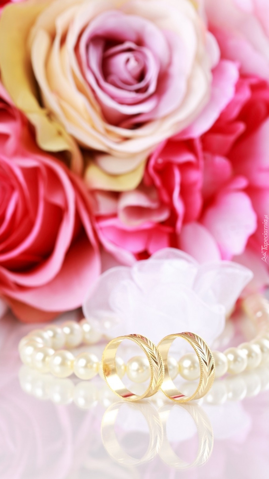 Złote obrączki obok pereł i róż
