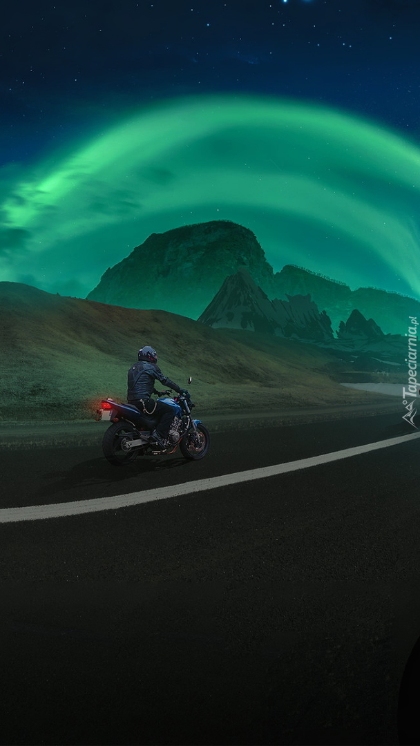 Zorza polarna nad górami i motocyklista na drodze