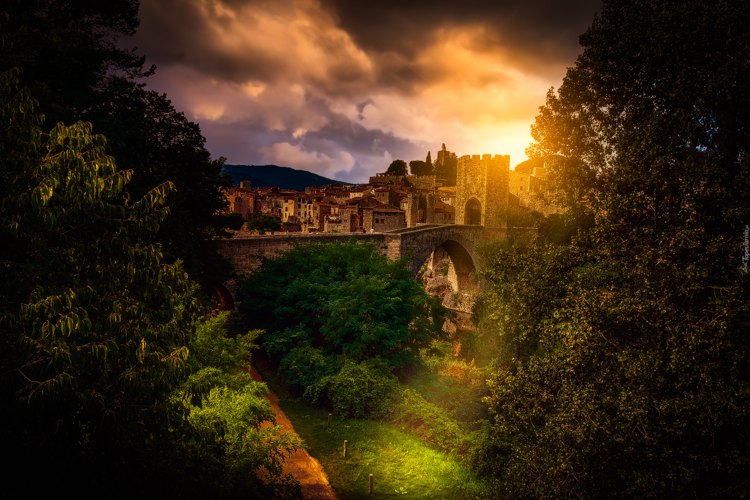 Hiszpania, Miejscowość Besalu, Most Puente de Besalu, Domy, Wzgórza, Drzewa, Roślinność, Wschód słońca, Chmury