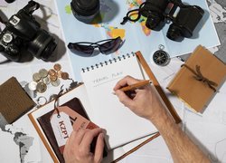 Aparat fotograficzny i ciemne okulary obok notatnika i mapy