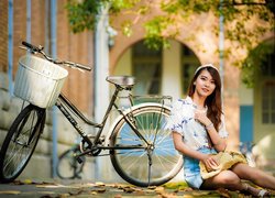 Azjatka siedząca obok roweru na ulicy