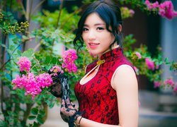 Azjatka w czerwonej sukience przy kwitnącym krzewie