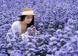 Azjatka w kapeluszu pośród niebieskich kwiatów