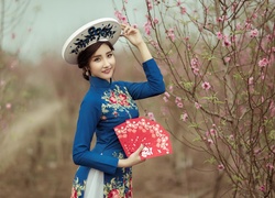 Azjatka w stylowym kapeluszu i z wachlarzem obok kwitnącego drzewa