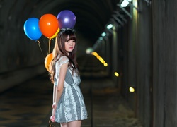 Azjatka z kolorowymi balonami na wstążkach w tunelu