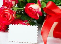 Biała kartka oparta o róże obok prezentu