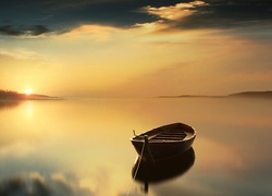 Blask zachodzącego słońca pada na łódkę na jeziorze