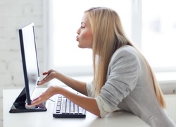 Blondynka siedząc przed monitorem przesyła buziaki