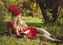 Blondynka w czapce czyta książkę zajadając jabłko
