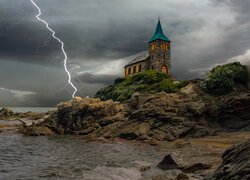 Błyskawica obok kościoła na skałach nad morzem