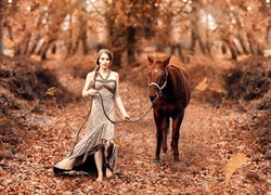 Bosonoga kobieta prowadzi konia przez jesienny las