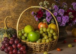 Bukiet astrów obok koszyka z owocami