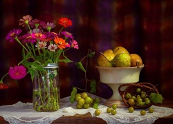Bukiet cynii w słoiku obok gruszek i winogron w kompozycji